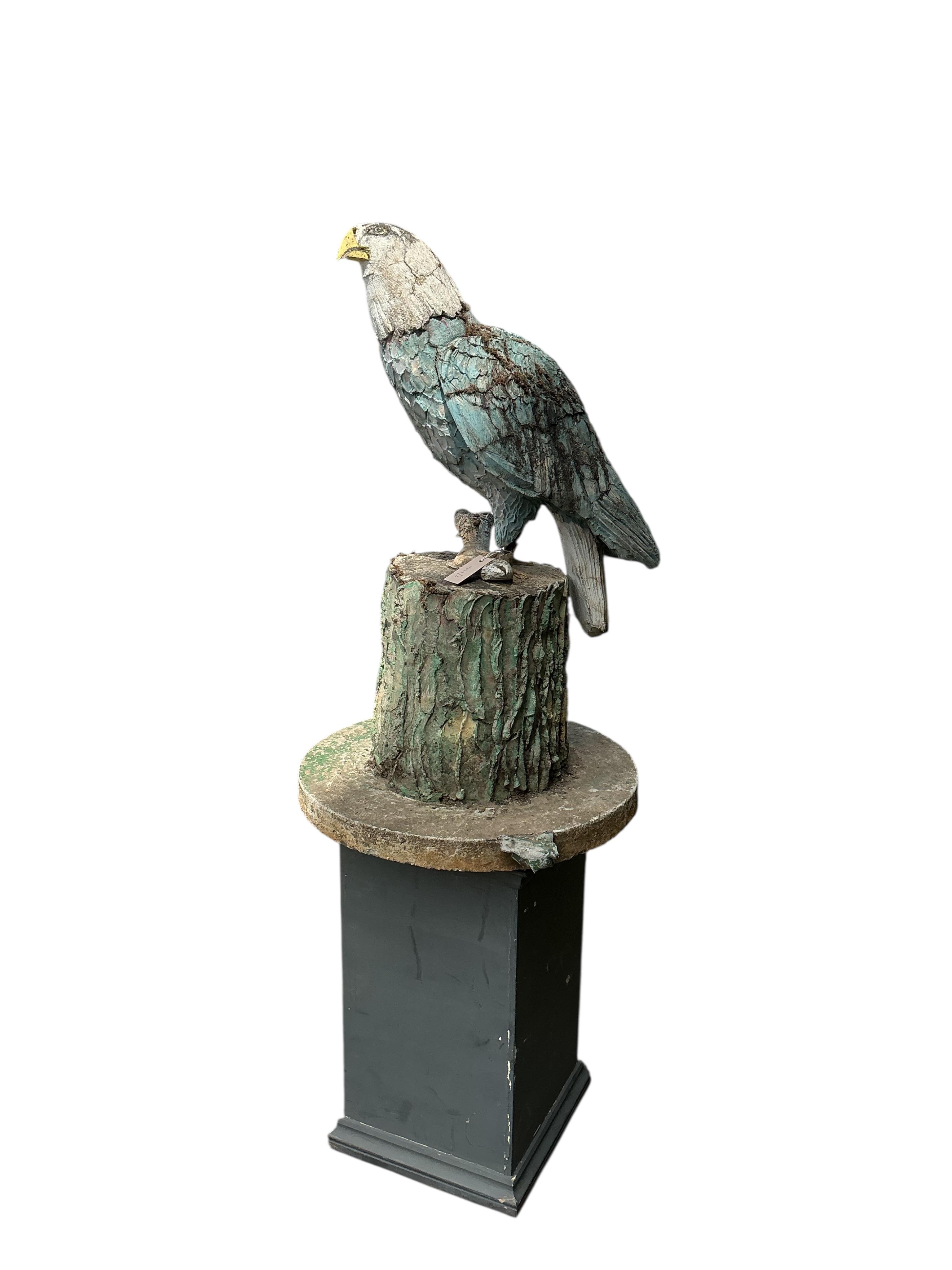 A cast stone garden ornament of an eagle perched on a stump with a salmon in its talons, on square wood plinth, height 150cm